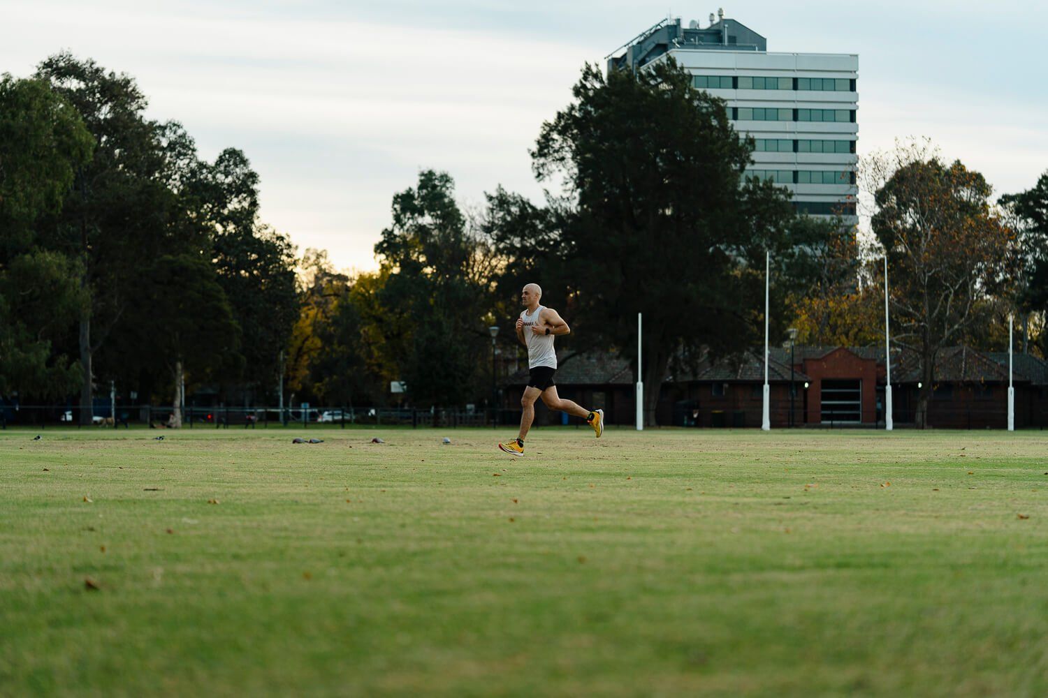 Dan running across a wide green oval in a Melbourne park